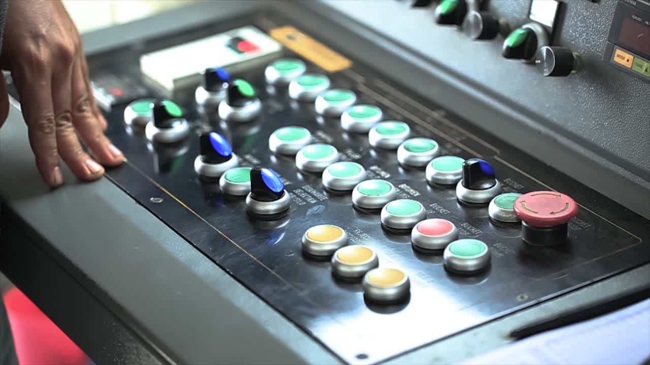 Worker's hands operate the asphalt mixing plant machine controller in the Asphalt Control Unit room, which functions to control the supply of asphalt to the mixing tool or pugmill