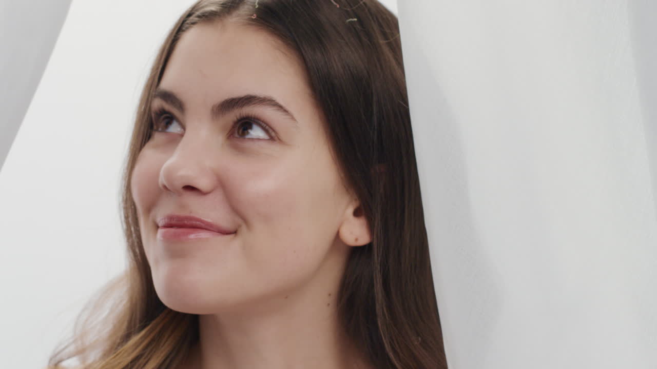 retrato en cámara lenta hermosa joven pétalos de rosa cayendo sobre atractiva mujer sonriendo disfrutando del lujo entre las sábanas en fondo blanco concepto de belleza