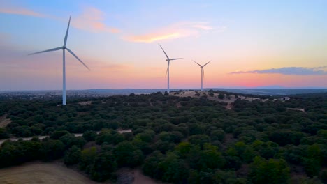 El-Deslizamiento-Aéreo-De-Las-Coloridas-Turbinas-Eólicas-Se-Dispara-Al-Amanecer-Sobre-Un-Bosque-Verde-Denso-Y-Profundo