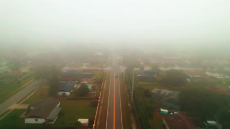 aerial reverse flyover of foggy and misty road through city of ocoee, florida with solo vehicle driving