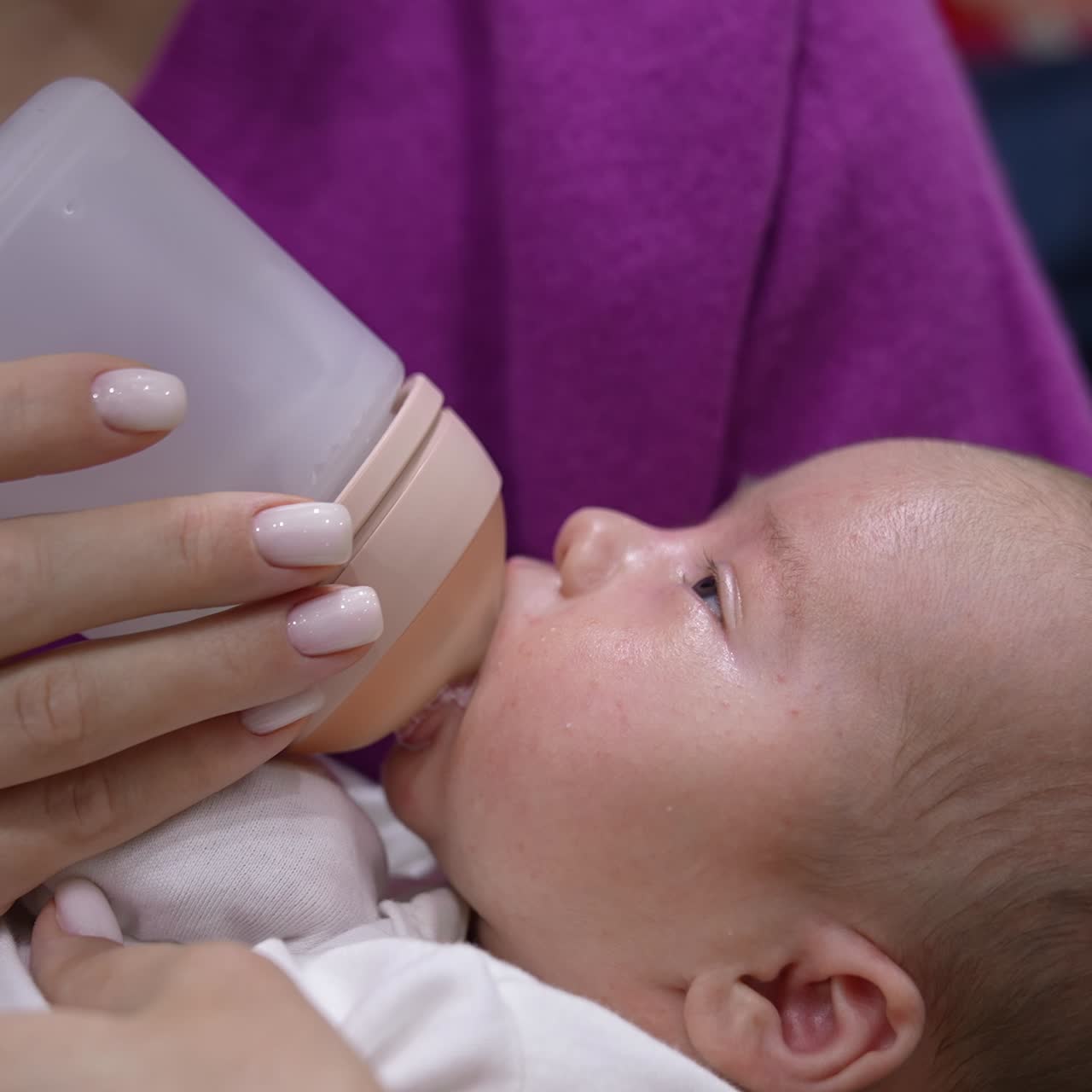 Sweet newborn baby is staying awake while being fed from bottle. Kid suckling milk from a bottle and looking at his mommy. Close up
