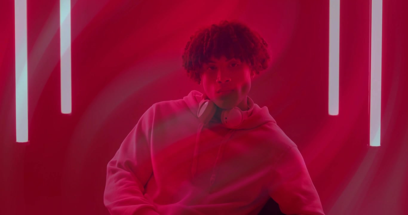Uomo che entra in uno studio illuminato di rosso e fiancheggiato da neon, indossando cuffie e gesticolando durante una demo tecnologica audio