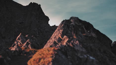 a closeup of dark rugged rocks with patches of dry grass and lichen against the pale blue sky