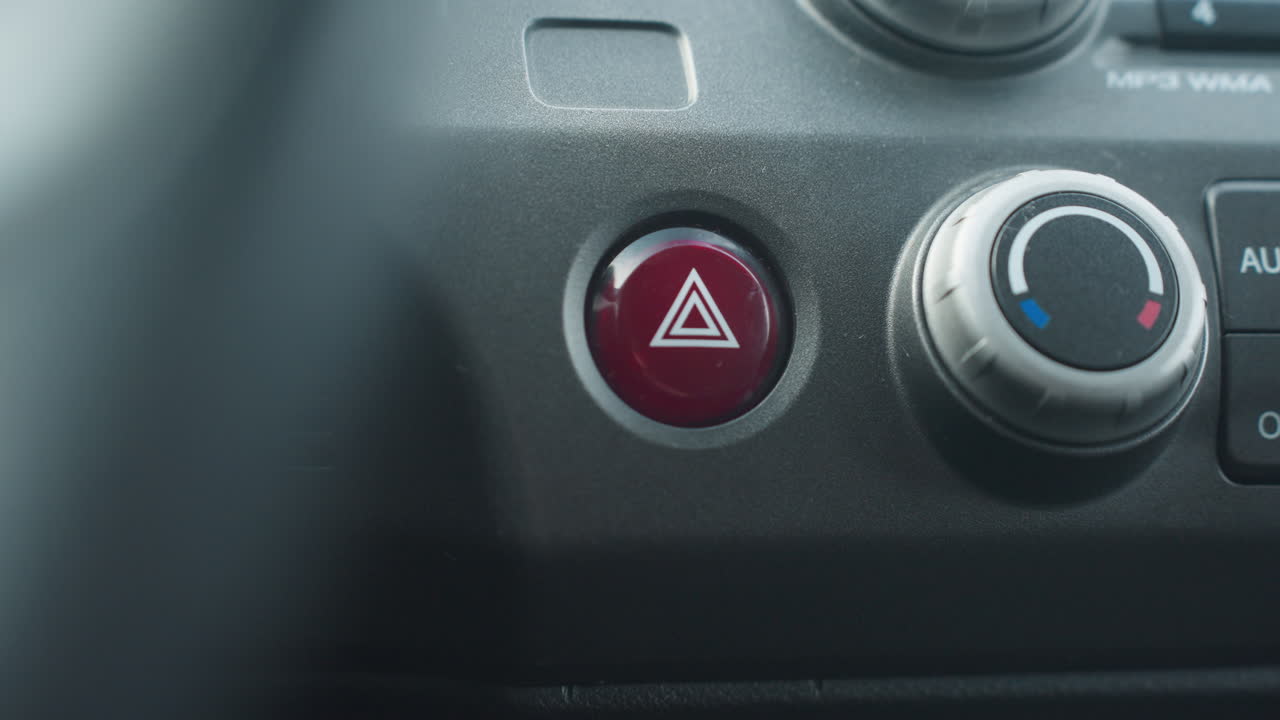 Close up of individual pressing hazard button on car dashboard interior showing finger interaction with emergency switch near climate dial triangular symbol and modern vehicle cabin lighting
