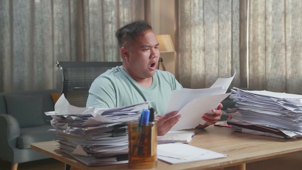 Fat Asian Man Yawning While Working Hard With Documents At The Office