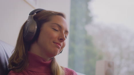 woman with prosthetic arm and hand wearing wireless headphones listening to music sitting on sofa