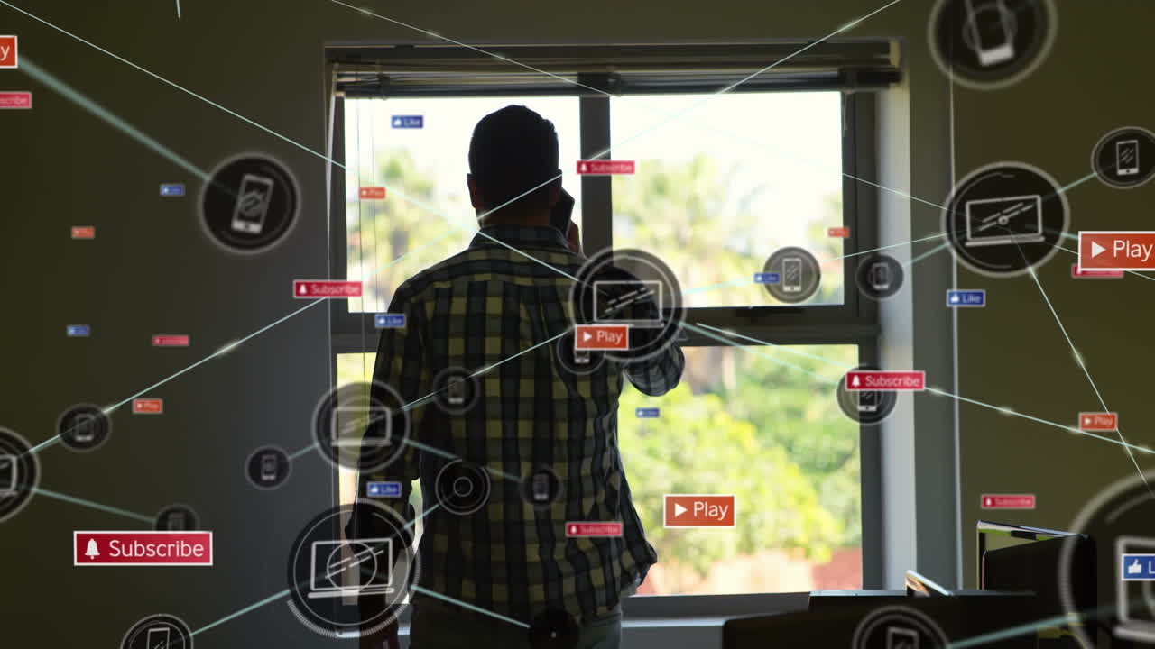 Animation of digital and social media icons against rear view of man talking on smartphone at home