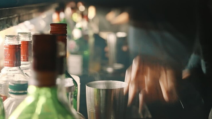 Mani di barista che versano e shakerano un cocktail in un bar buio.
