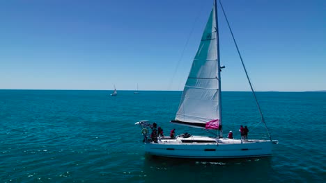 static aerial shot of a sailboat sailing past in a tropical ocean on a beautiful day