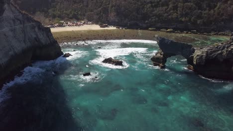 aerial view of atuh beach on nusa penida, indonesia on a sunny day and with crystal blue water hitting the rock formations