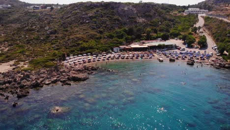 wide aerial view of anthony quinn bay with its azure blue waters and a great beach full of umbrellas and sun beds with the bars and restaurants in the background