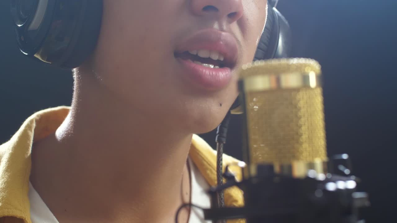 검은색 배경 에 있는 콘덴서 마이크 로 노래 하는 어린 소년 의 입 의 근접