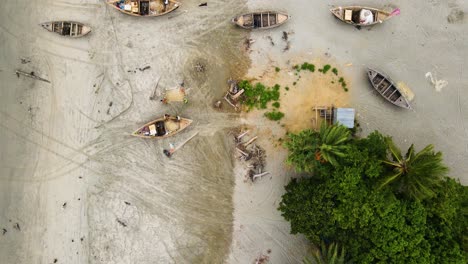 fishermen with wooden boats repairing their fishing nets in tropical shoreline of kuakata sea beach, bangladesh