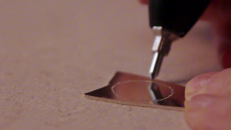 Primo piano dell'incisione di un cerchio su un pezzo d'argento utilizzando un utensile Dremel. Perfetto per la creazione di gioielli, la lavorazione dei metalli e contenuti sull'artigianato