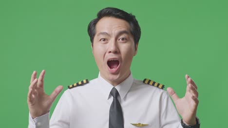 녹색 스크린 배경 스튜디오에 서있는 동안 미소 짓고 와우라고 말하는 아시아 남자 조종사의 클로즈업