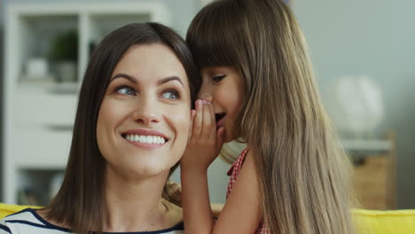 Close-Up-View-Of-Cute-Girl-Smiling-Whispering-Some-Secret-To-The-Ear-Of-Her-Young-Mother