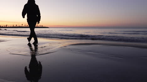 silueta de hombre caminando en la playa durante la puesta de sol, saltando sobre un charco