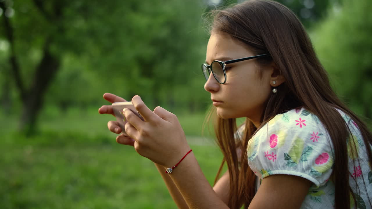 Adolescente séria enviando mensagem no celular em uma floresta verde.