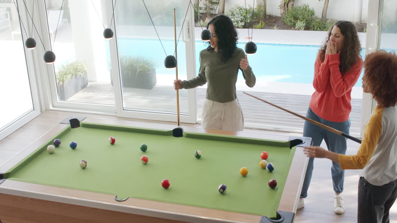Female friends aiming shot on pool table, striking ball into pocket and celebrating, copy space