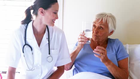 Ärztin-Serviert-Einer-älteren-Frau-Im-Schlafzimmer-Ein-Glas-Wasser