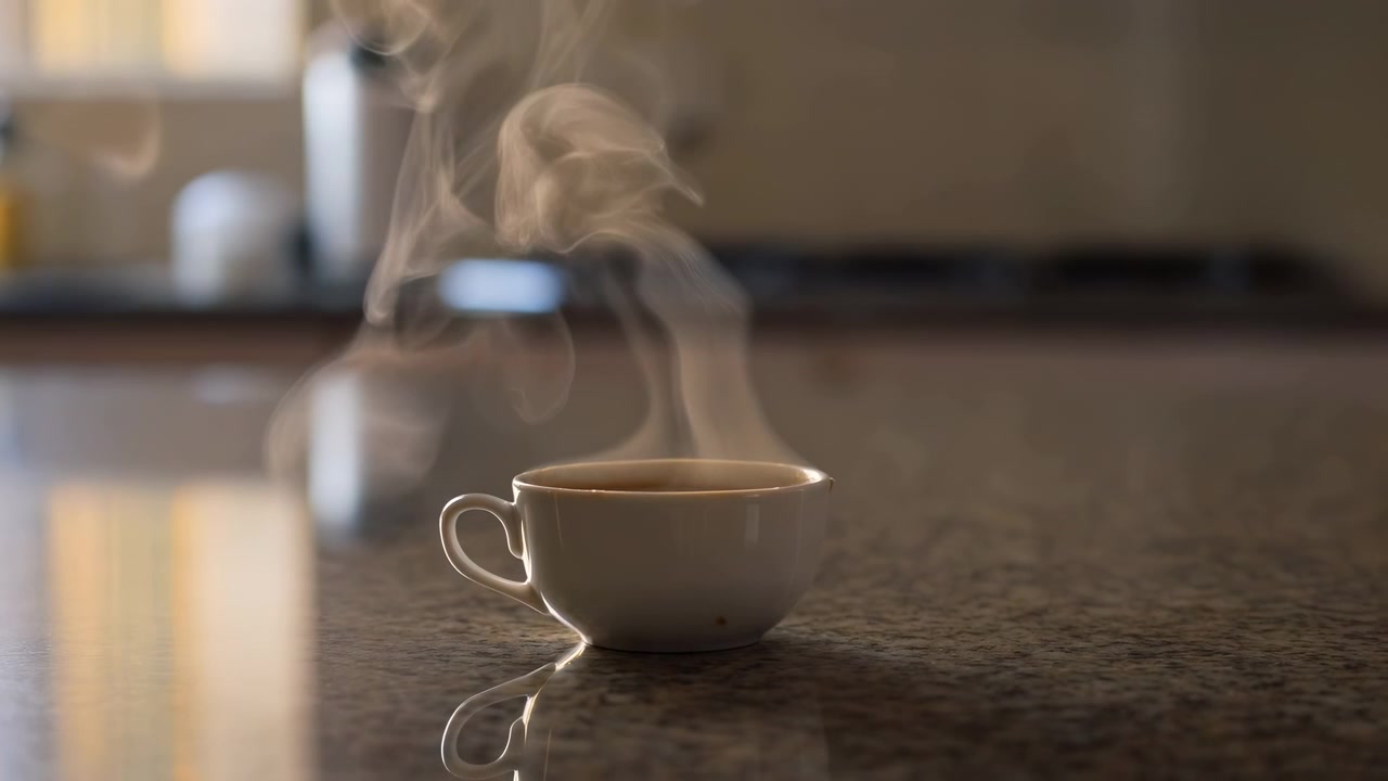 Una taza de café humeante se coloca sobre una encimera reflectante en una cocina o comedor moderno, creando un ambiente cálido y acogedor. El ángulo de primer plano, ligeramente elevado, resalta la C