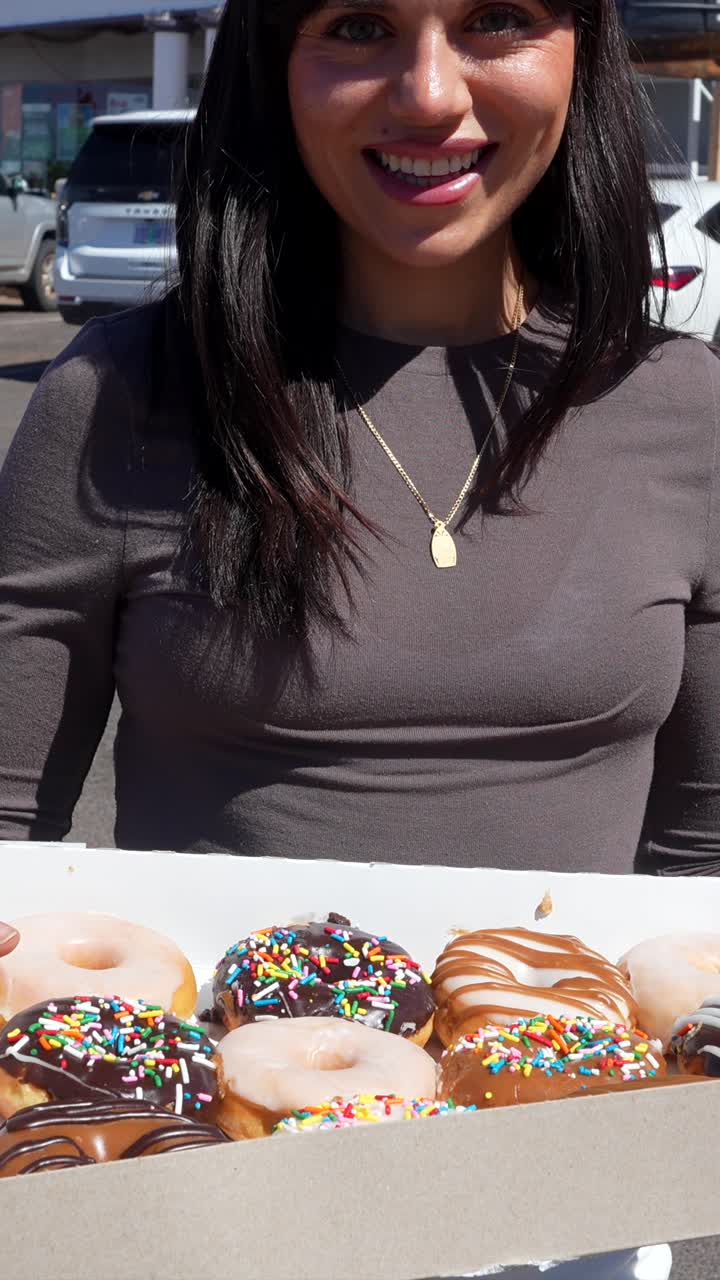 Smiling Woman Holding a Box of Assorted Colorful Donuts