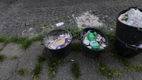 overflowing garbage bins on a cobblestone street