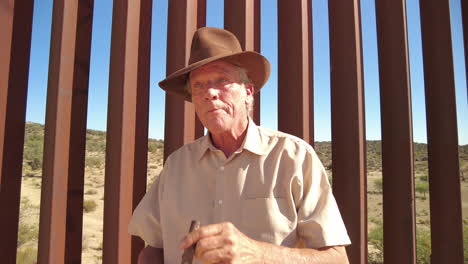 american male guy with fedora hat lights cigare devant nous mexico border fence