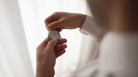 close up of groom checking vintage pocket watch in soft natural light