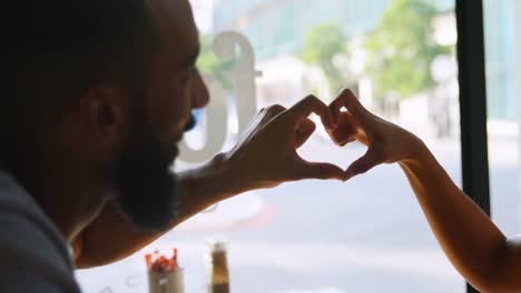 side view of young mixed-race couple forming heart shape with hands in cafe 4k