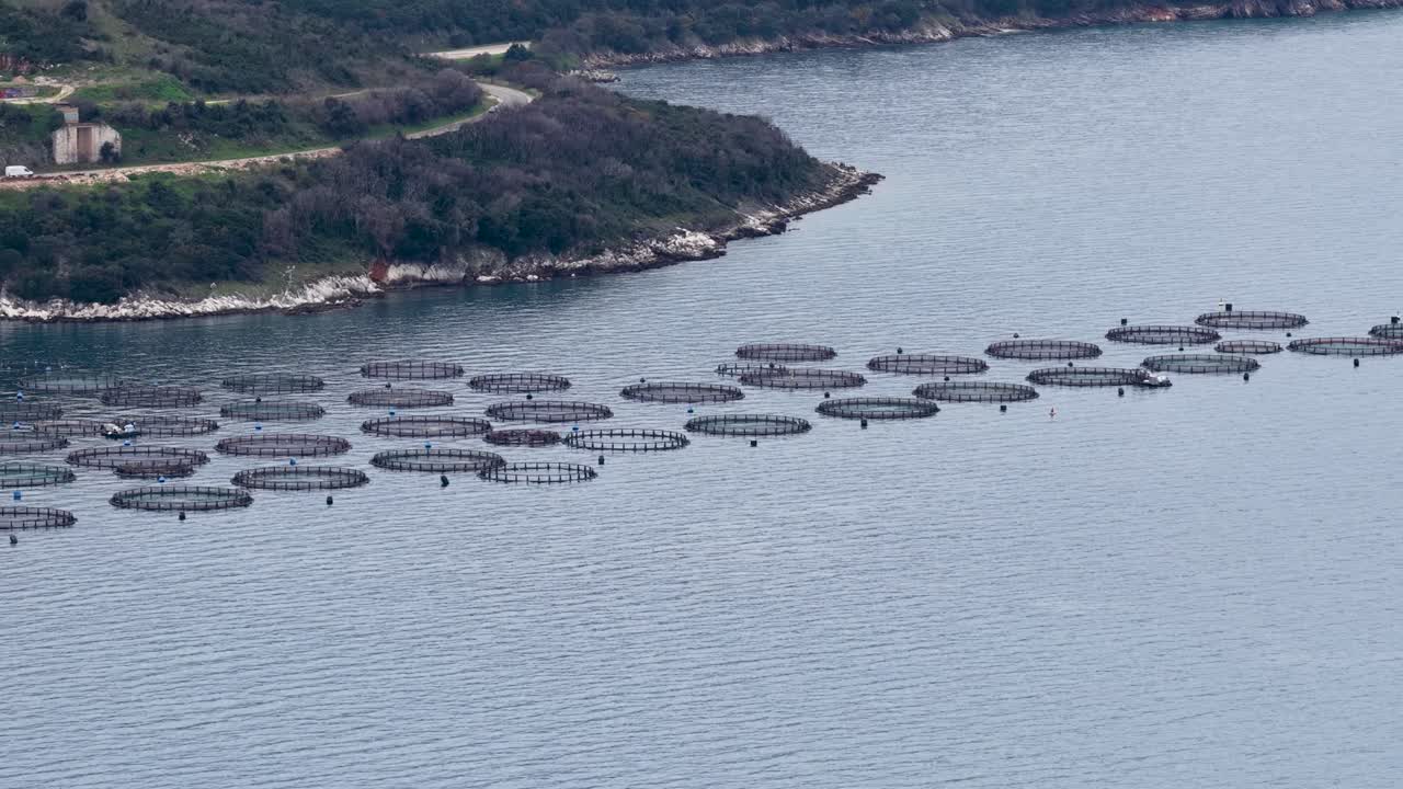 Luftfoto af stort fiskeopdræt med dambrug, der flyder i blåt hav nær kysten