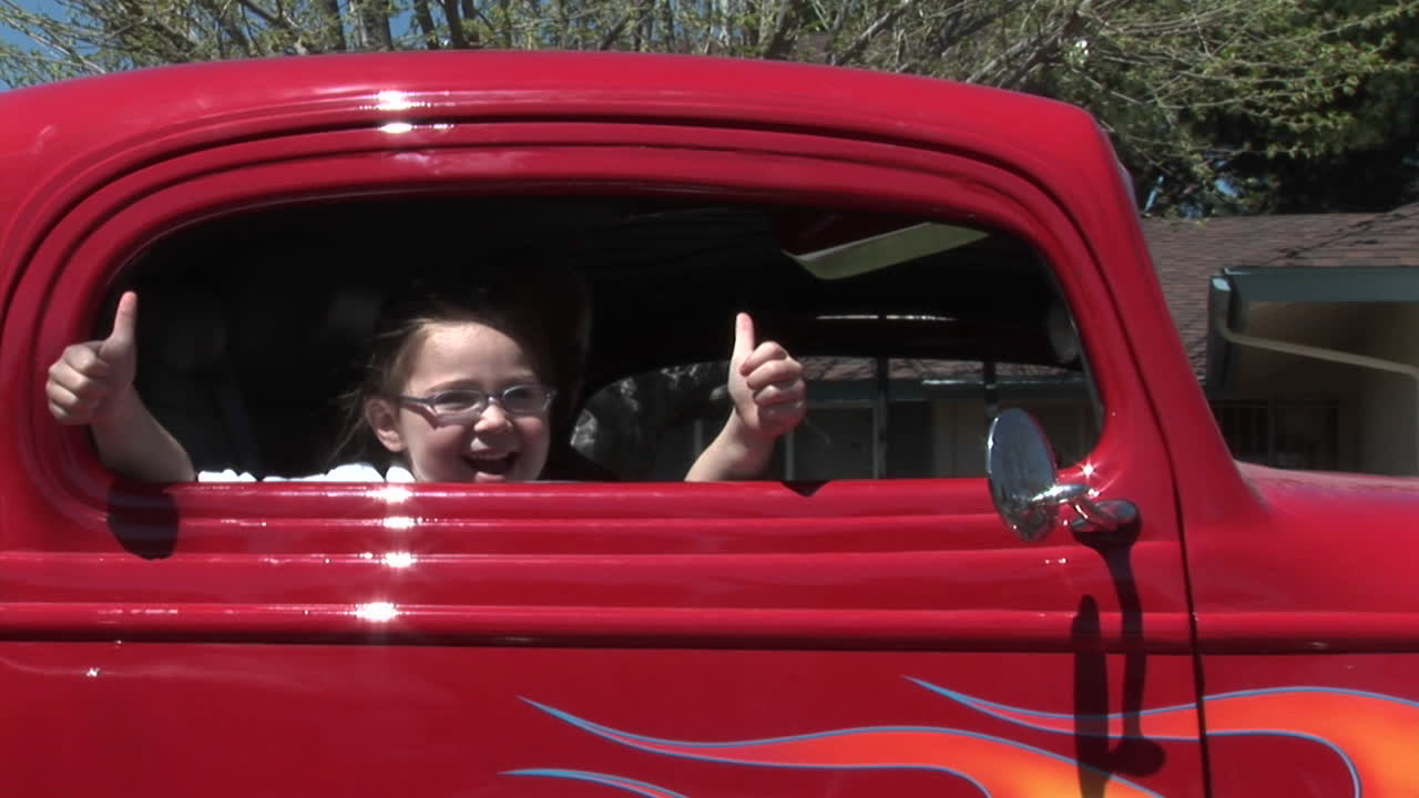 una niña da dos pulgares hacia arriba por la ventana de un auto