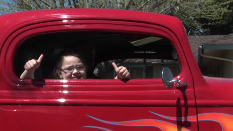 a young girl gives two thumbs up out a car window