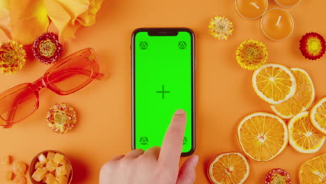 orange themed flat lay with phone and green screen