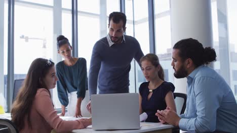 grupo diverso de colegas creativos masculinos y femeninos reunidos en una mesa con una computadora portátil en discusión