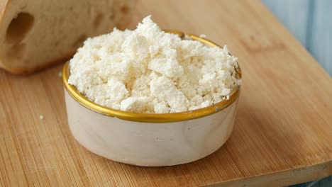 cerrar el queso cottage en un tazón en una tabla de madera con un pedazo de pan