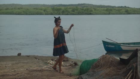 a woman with dark hair working on a fishing net next to a lake