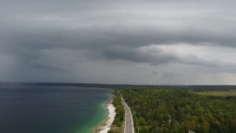 Aerial-view-of-a-highway-next-to-a-white-sandy-coastline-under-looming-dark-storm-clouds