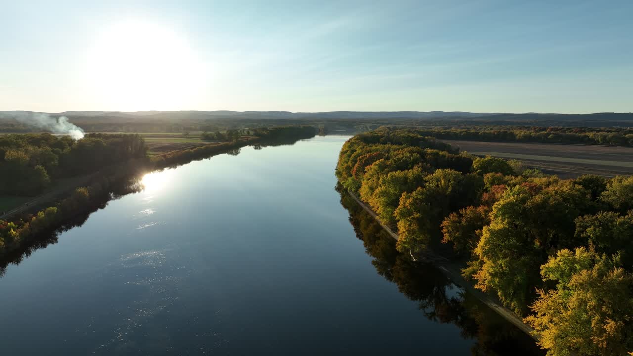 Slow drone flight over tranquil Connecticut River in Hadley Massachusetts at golden sunset. Colorful trees and plants during fall season. Beautiful autumn day in scenic area of USA. Wide shot.