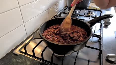 mujer revolviendo hígados de pollo en una estufa de gas para hacer paté de hígado de pollo