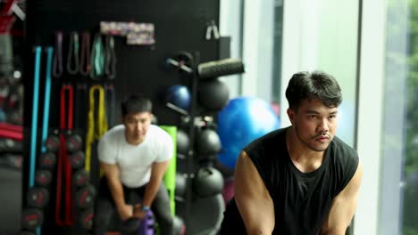 Two men perform kettlebell swings in a well-equipped gym with natural lighting