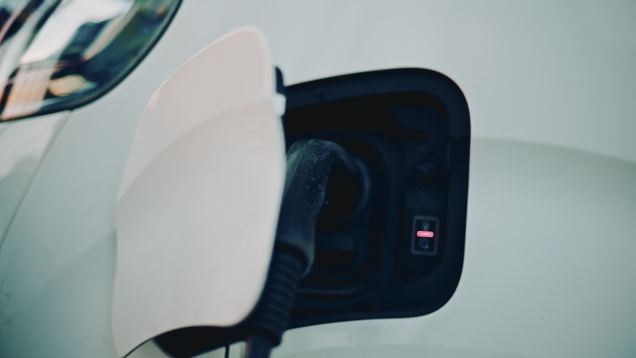 Electric vehicle charging in warm sunset light, focusing on the plug inserted into the charging port with soft bokeh