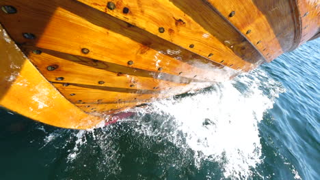 front of a traditional wooden boat, sjekte sailing on the blue ocean with water splashing in arendal, norway