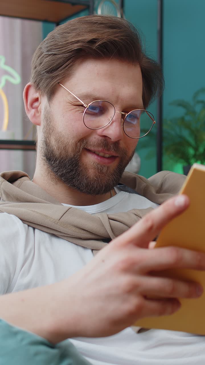 Ung mand slapper af og læser interessant bog, der vender sider, smiler og nyder litteratur og hviler sig på sofaen