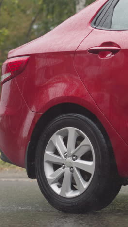 stylish red car drives on asphalt road in city in heavy rainy summer weather. modern automobile moves on street against old buildings under pouring rain closeup