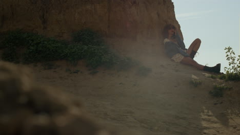 relaxed woman leaning sand cliff relaxing on seashore. girl sitting in shadow.