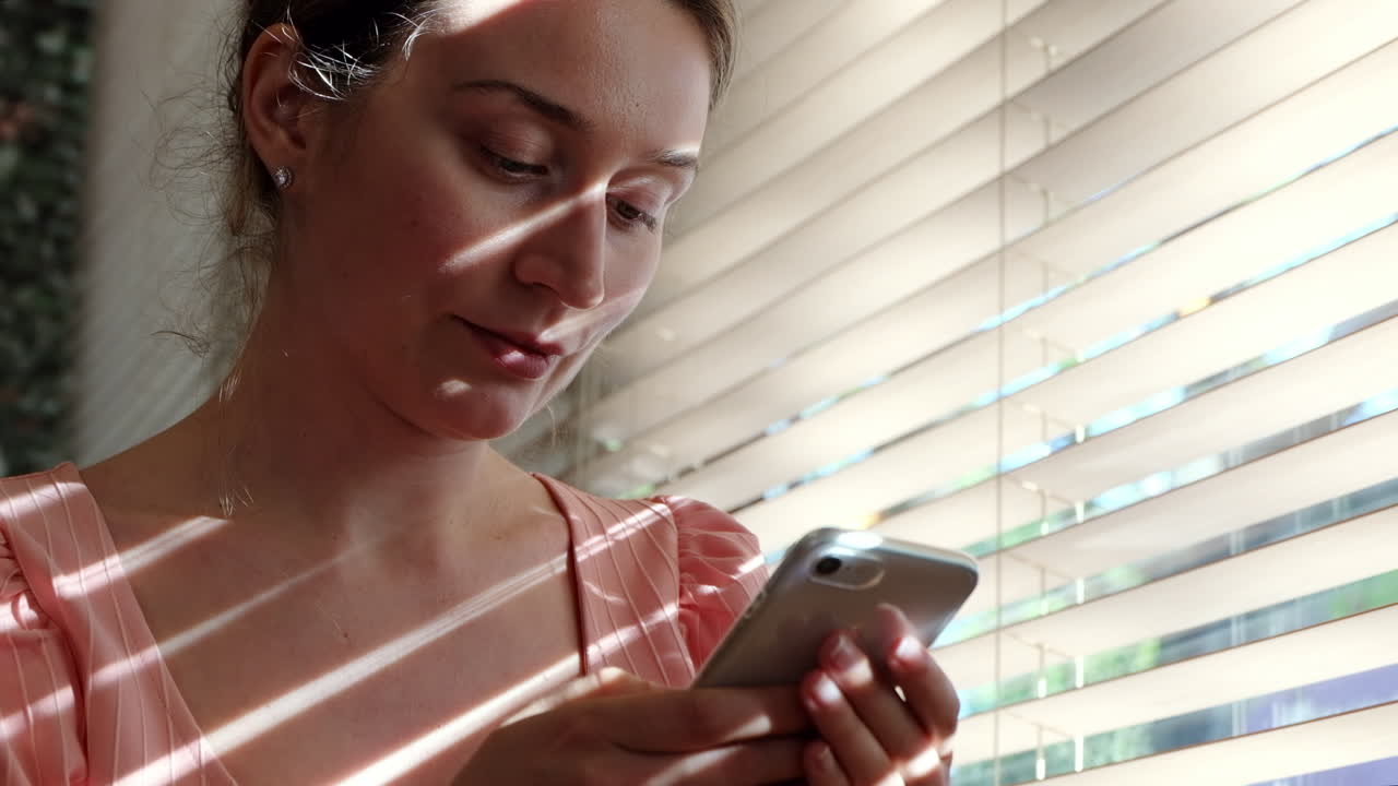 Woman texting on her phone near a window