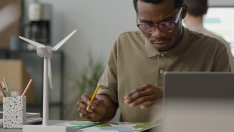 homme d'affaires utilisant un ordinateur portable assis à table avec un modèle de moulin à vent au bureau 2