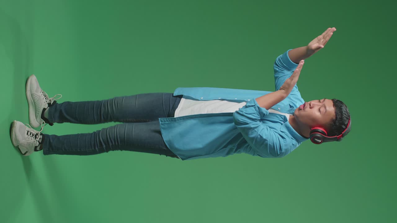 Full Body Of Young Asian Boy Listening To Music With Headphones And Dancing In The Green Screen Studio