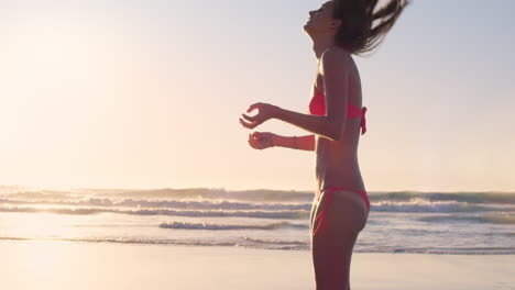 woman flicking hair back on beach at sunrise